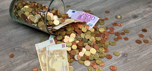 A glass jar with euro coins and banknotes spilled on a wooden surface, representing finance and savings.